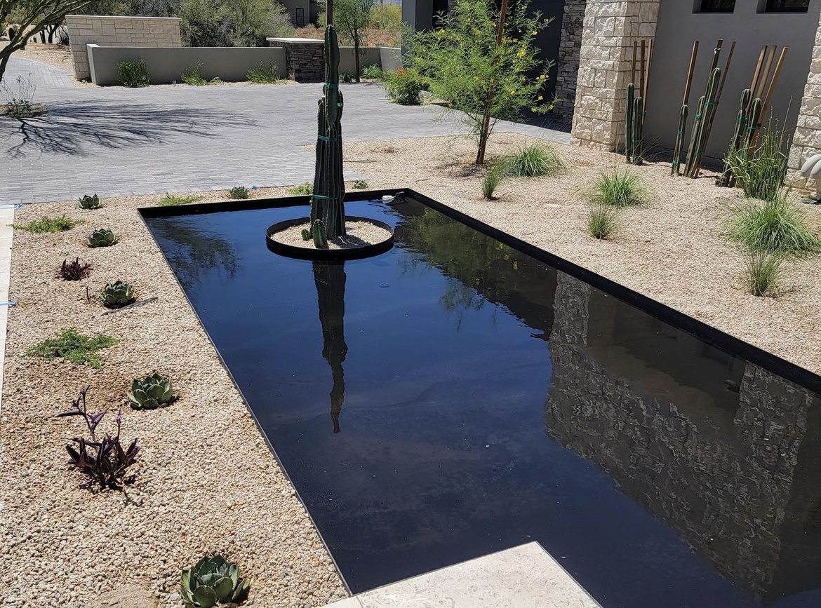 Front-facing aerial view of luxury desert estate with stone façade, black metal roofing, and desert terrain.