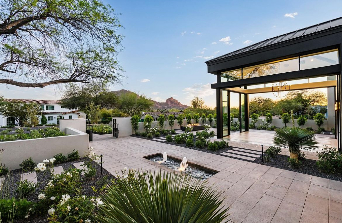 Elegant outdoor courtyard with fountains, lush landscaping, and mountain views, featuring a modern glass-walled pavilion.